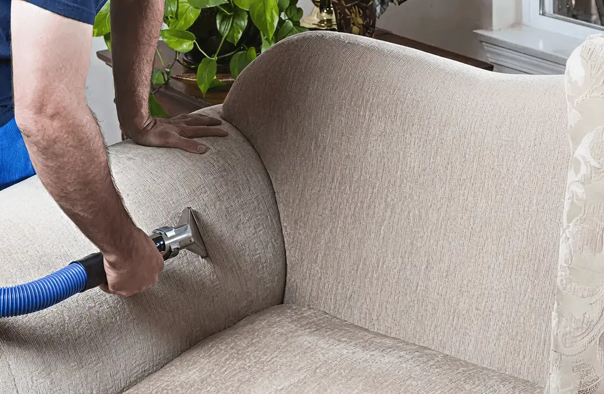 Professional upholstery cleaner deep-cleaning a fabric sofa with a handheld extraction tool and hose, New Orleans, LA.